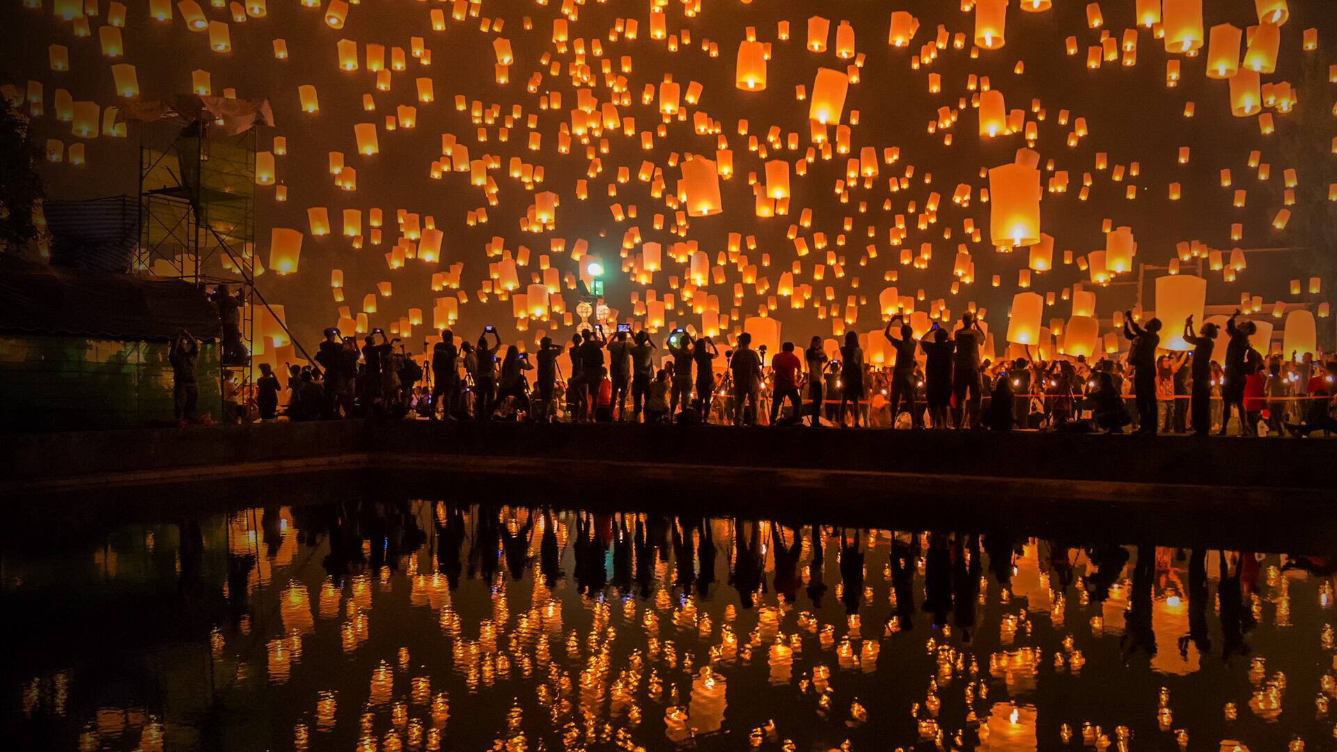 Thousands of Lanterns in the sky with the reflection on the water with people watching.Yeepeng festival, Chiangmai