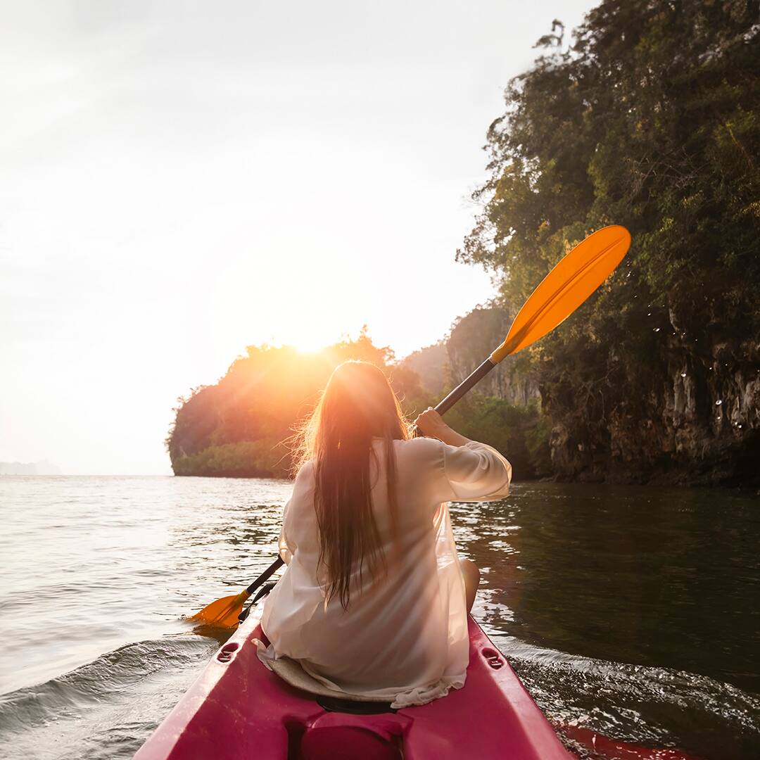 Woman kayaking on the sea with sunset over mountain. Asian woman rowing on the river