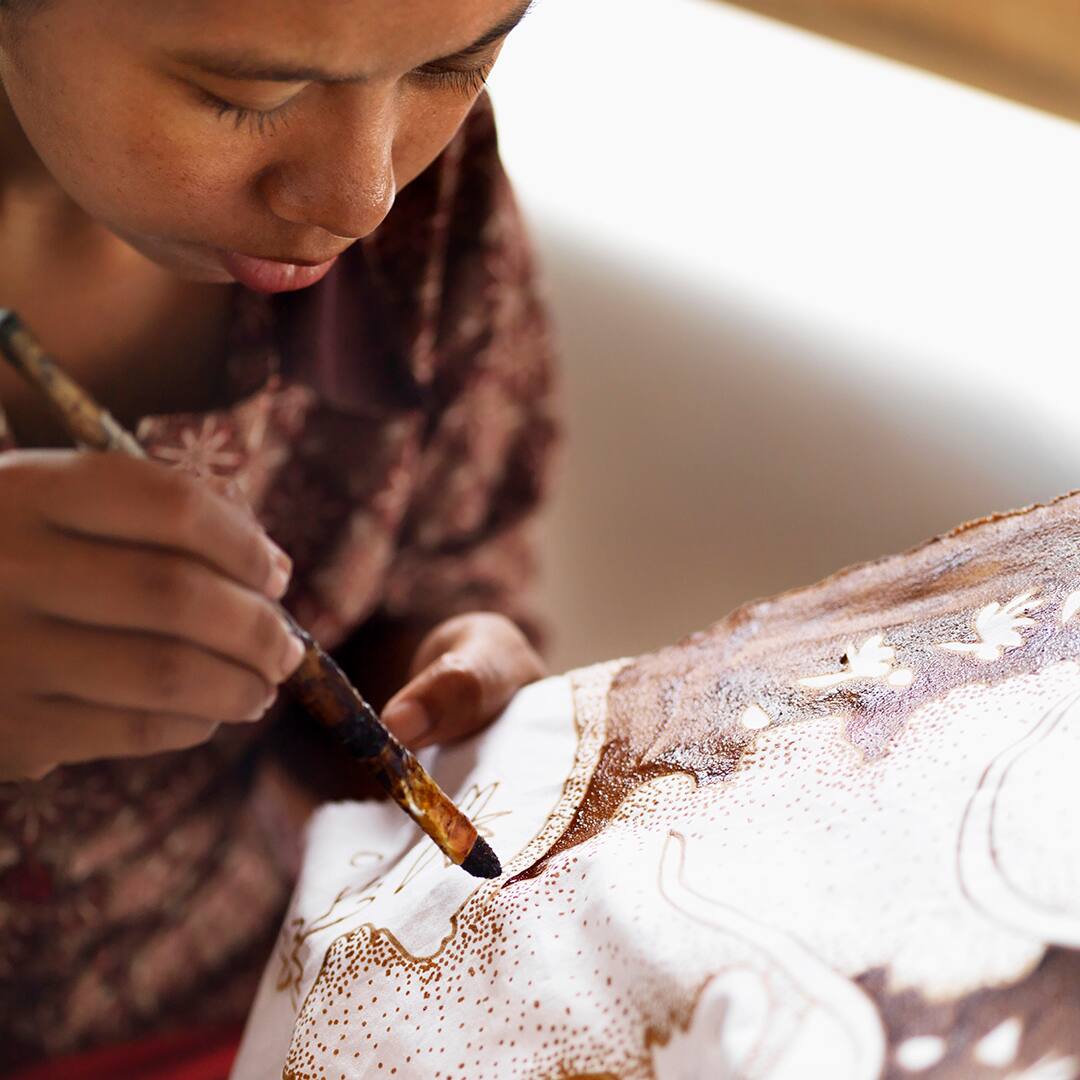 Batik artist applying liquid wax to fabric using a paintbrush