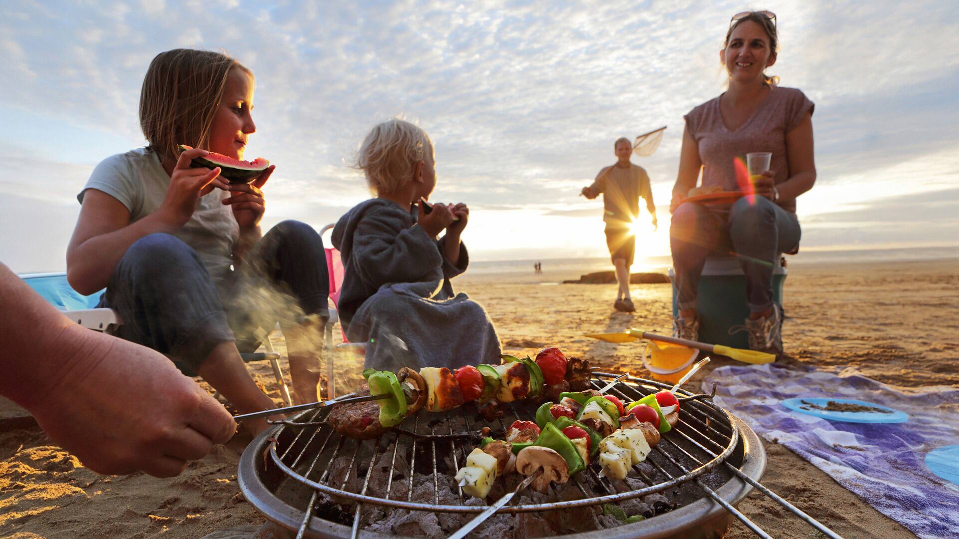 Family having BBQ on beach at sunset