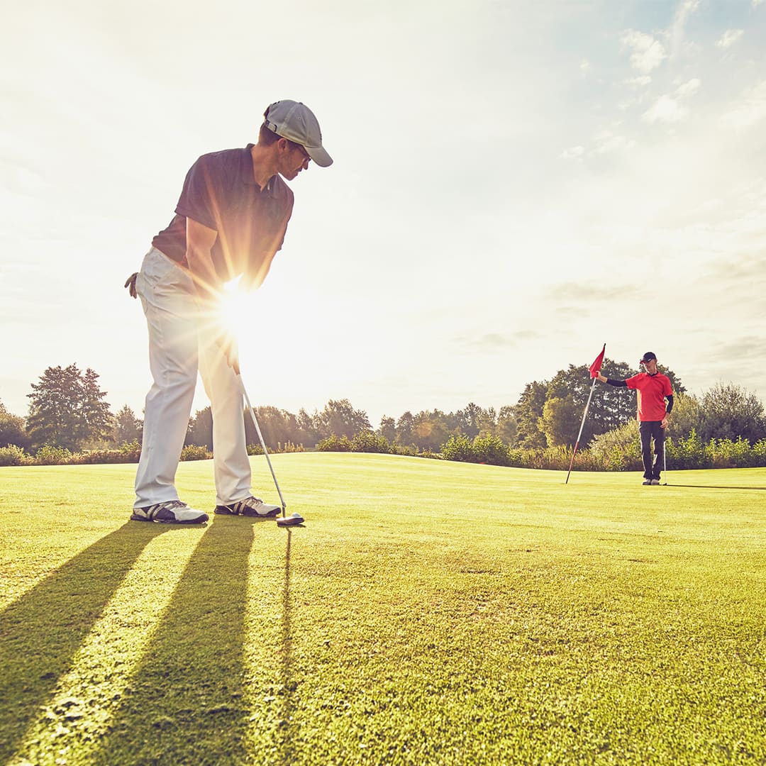 Mid-adult men playing golf at sunset
