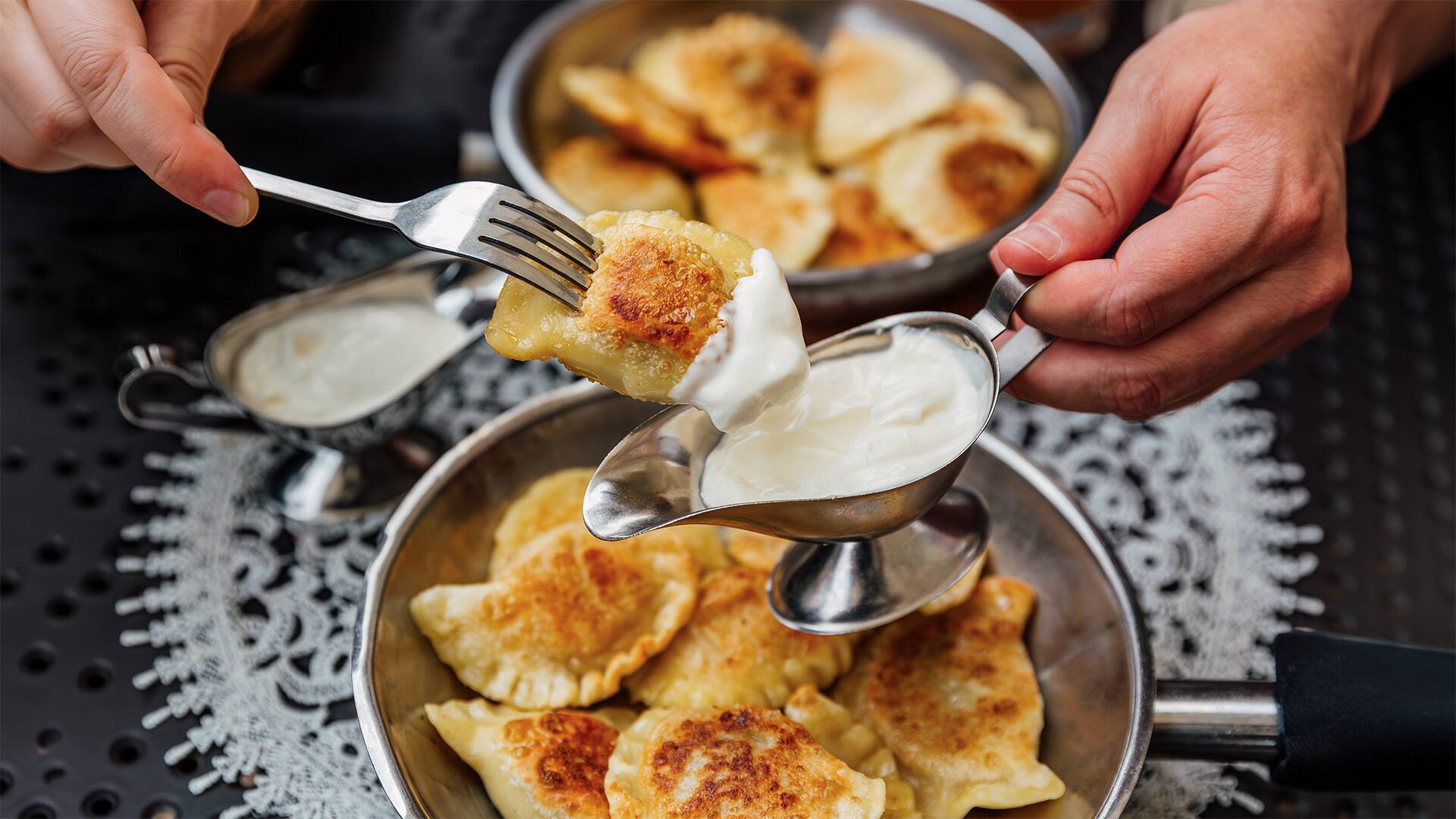 Man dipping pierogi dumplings in sour cream, close-up