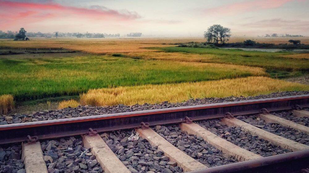 pink skies and railway track and green fields in india