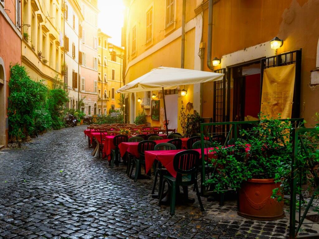 table and chairs outside cafe on pretty cobbled street in trastevere neighbourhood of rome in italy