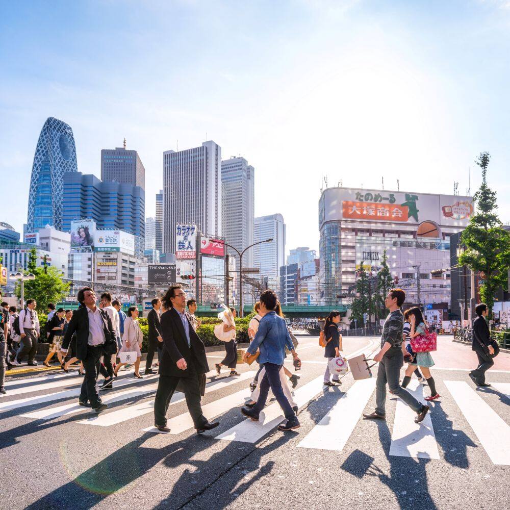 people walking over a crossing with skyscrapers in the background tokyo japan