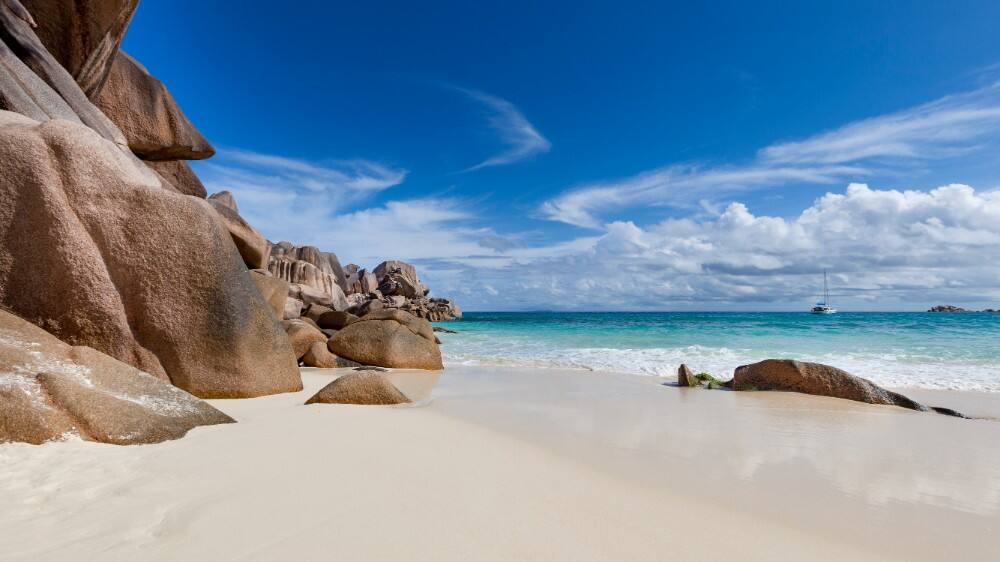 white sand beach and turquoise ocean with catamaran in seychelles