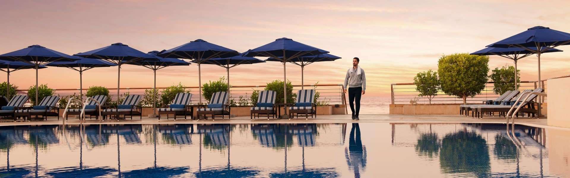 swimming pool surrounded by sun loungers and parasols at sunset