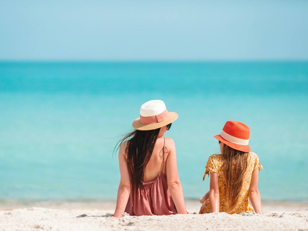 a woman and young daughter sitting on the sand at saadiyat beach in the uae gazing out to sea