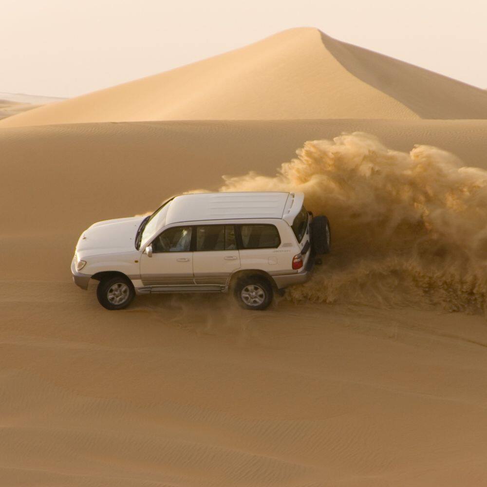 a four by four vehicle  driving through desert sand dunes in the uae 